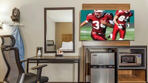 A hotel room with a desk, a chair, a refrigerator, a microwave, and a television displaying a football game. - Red Roof Inn Lumberton (Lumberton)