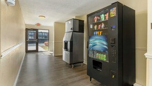 A hallway with a vending machine, a refrigerator, and an exit door. - Red Roof Inn Lumberton (Lumberton)