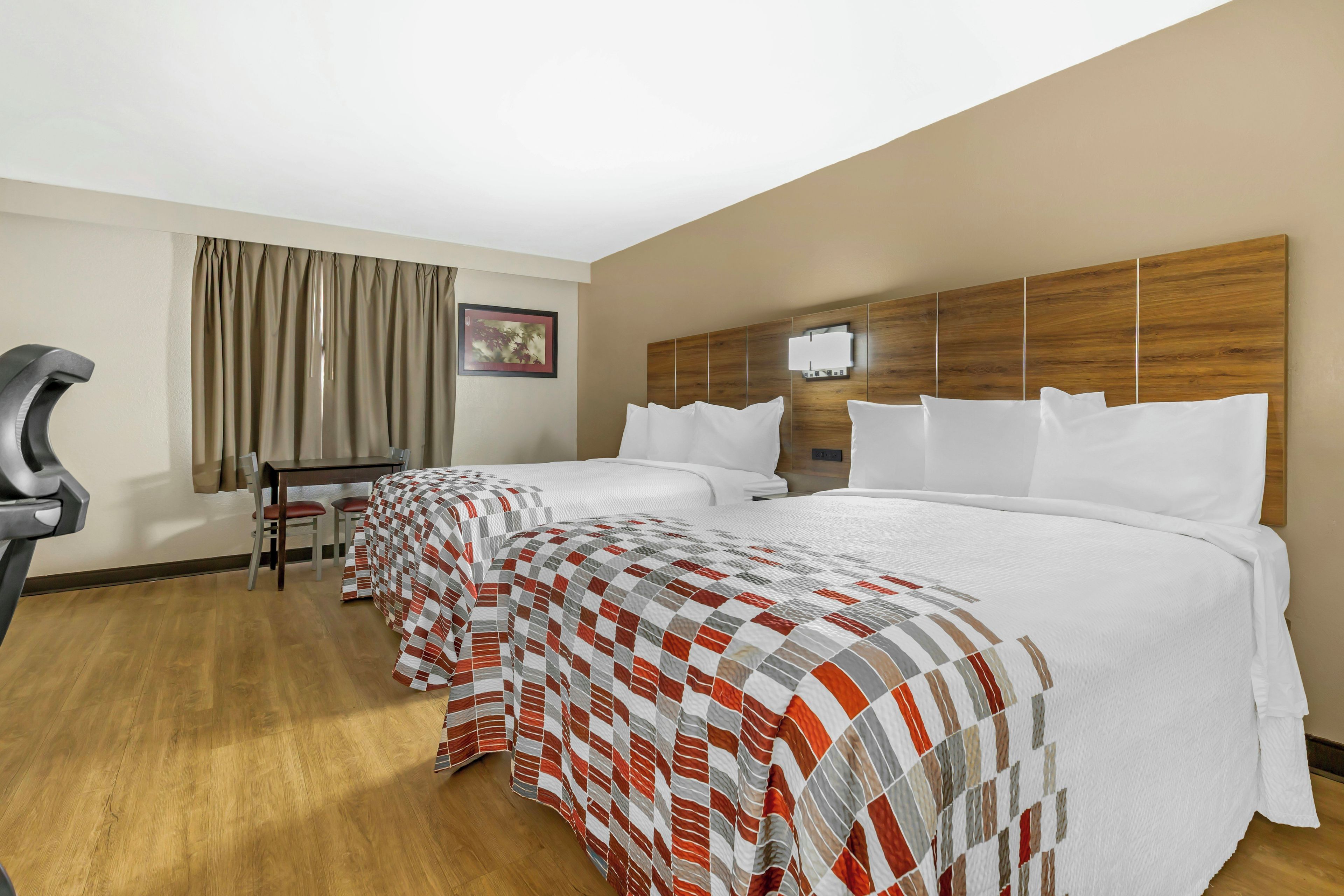 A hotel room with two beds, a desk, and a chair.