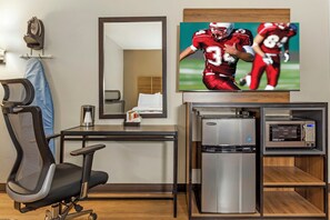 Une chambre d’hôtel équipée d’un bureau, d’une chaise, d’un réfrigérateur, d’un four à micro-ondes et d’un téléviseur diffusant un match de football.