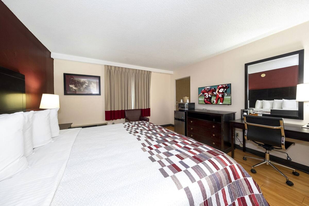Une chambre d’hôtel avec un grand lit, un bureau avec une chaise, une télévision et une fenêtre avec des rideaux.