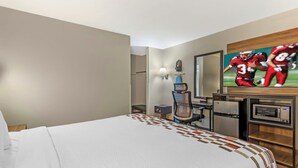 A hotel room with a large bed, a desk with a computer, a microwave, and a TV displaying a football game.