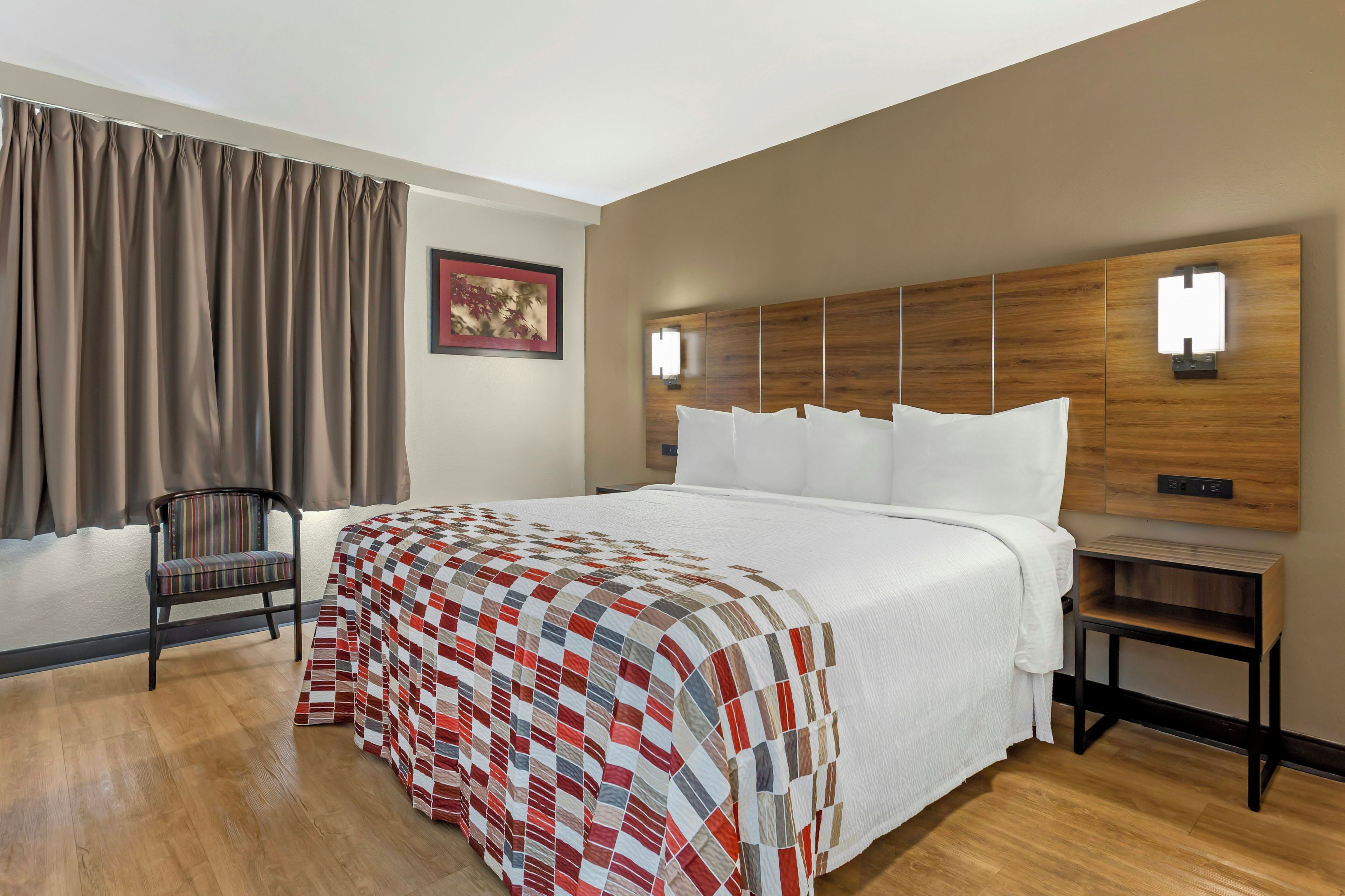 A hotel room with a large bed, a chair, a wooden headboard, and a nightstand.