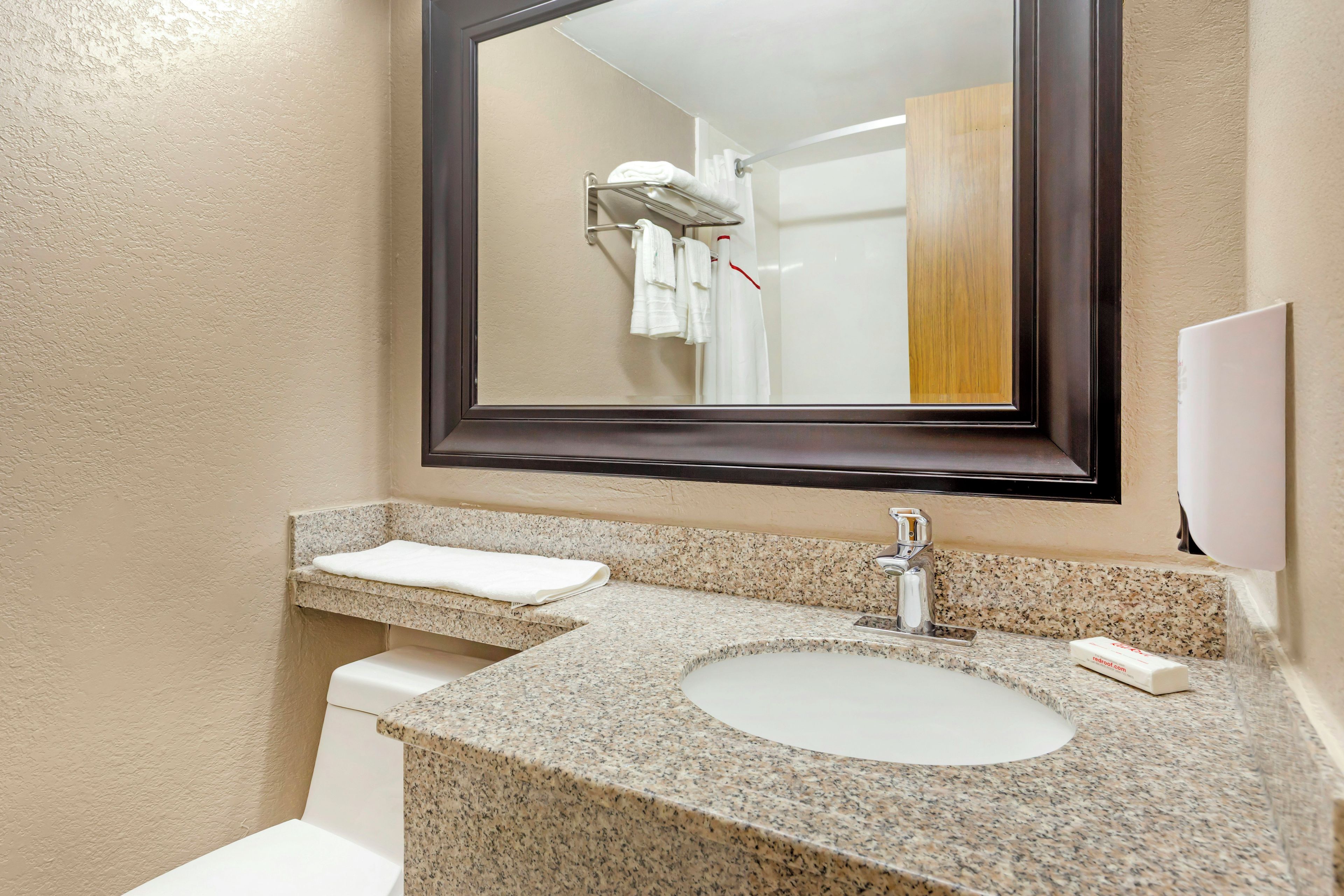 A bathroom with a granite countertop sink, a mirror, a towel rack, and a toilet.