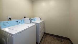 Pesuhuoneessa on kaksi Whirlpool-merkkiä olevaa pesu- ja kuivauskonetta, seinään asennettu pistorasia ja laatoitettu lattia.