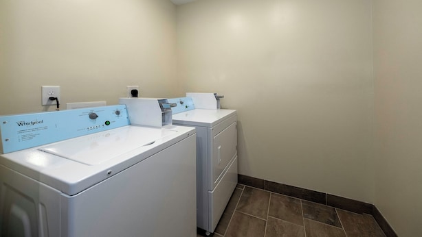 A laundry room with two Whirlpool washers and dryers, a wall-mounted electrical outlet, and a tiled floor.
