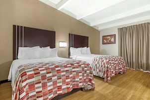 A hotel room with two beds, a ceiling light, a painting, and a window with curtains.