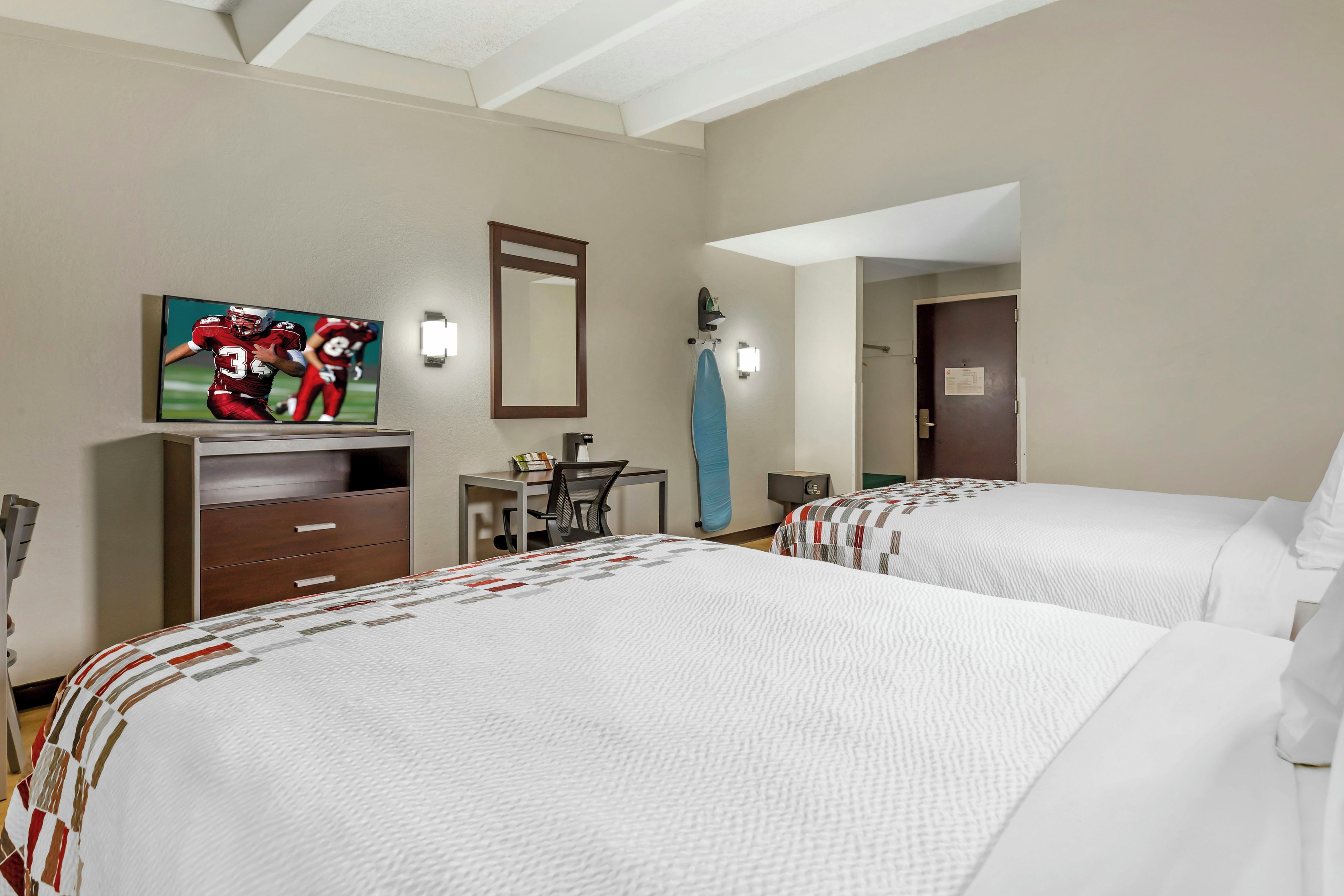 A hotel room with two beds, a desk, a chair, a television, and a mirror.