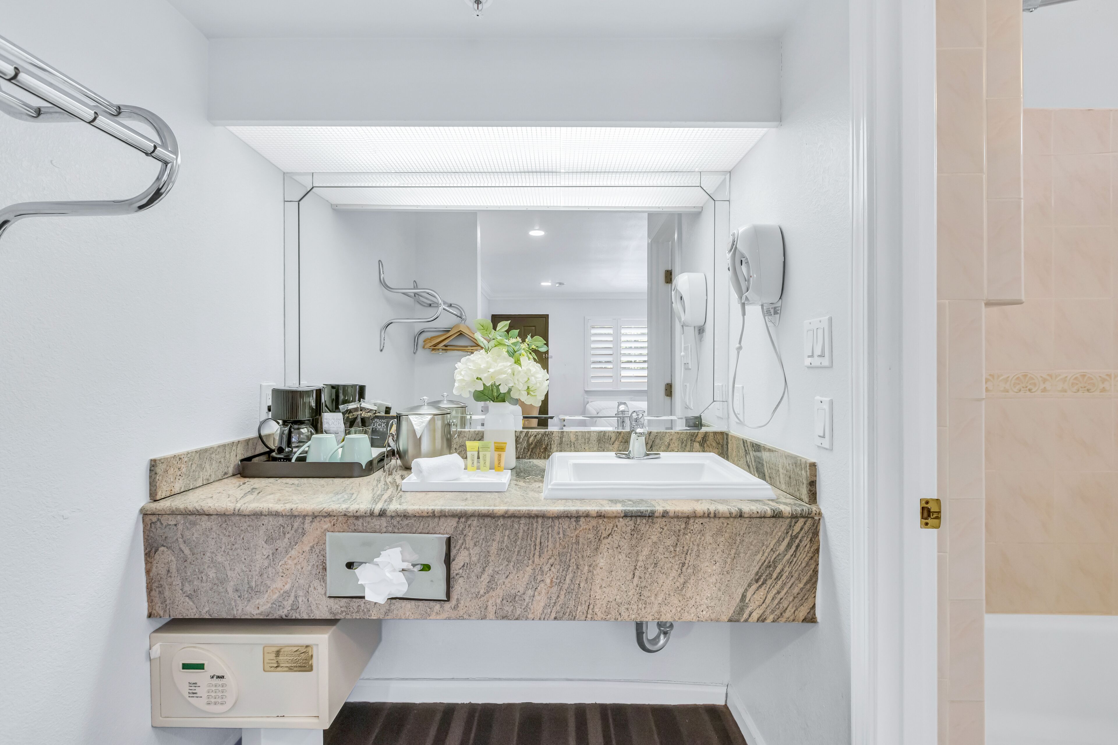 A modern bathroom with a granite countertop, a large mirror, a hairdryer, and a towel rack.