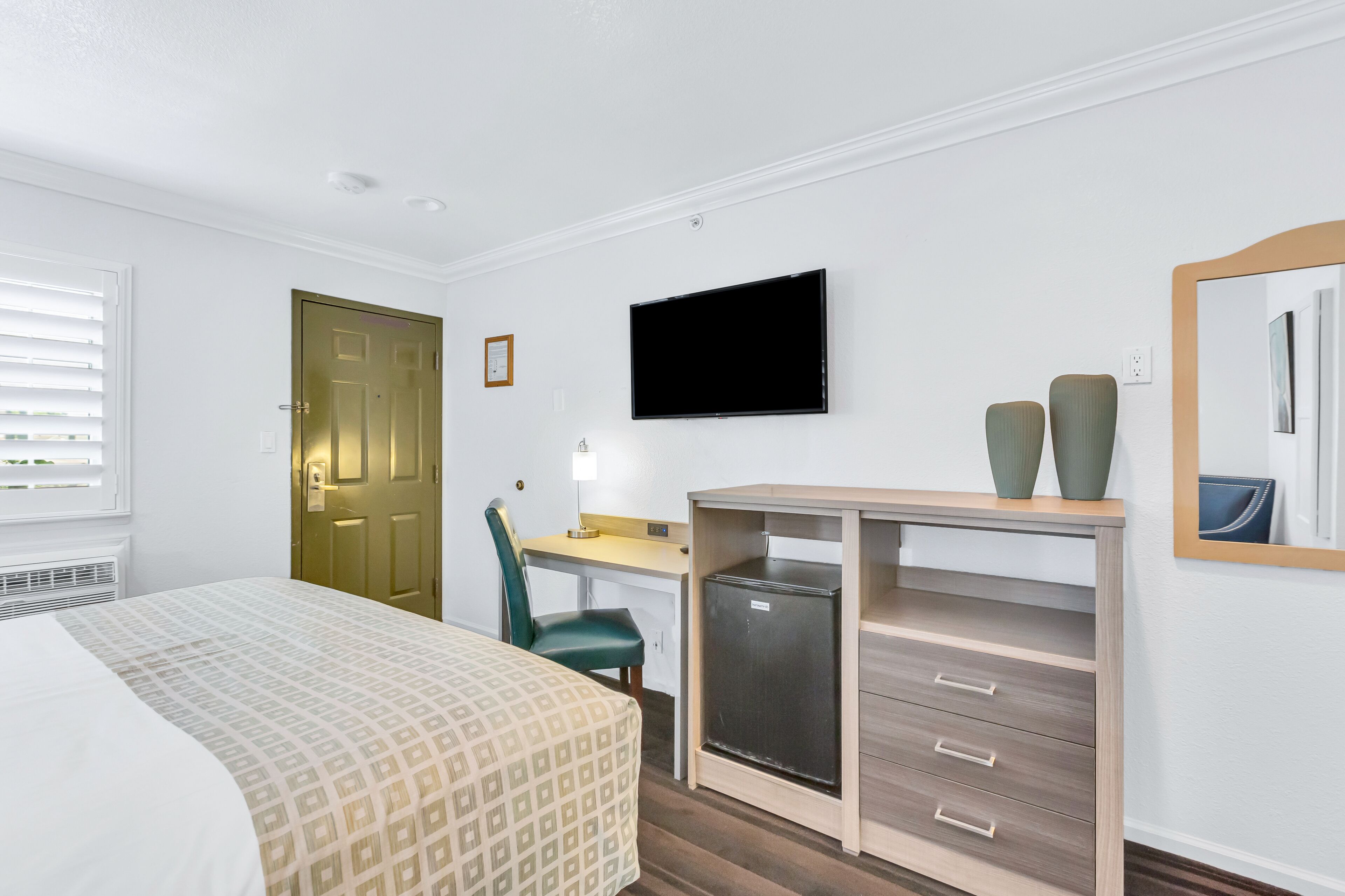 Une chambre d’hôtel équipée d’un lit, d’un bureau, d’une chaise, d’une télévision et d’un petit réfrigérateur.