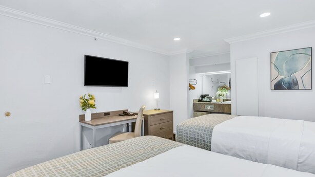 A hotel room with two beds, a desk, a chair, a TV, a mirror, and a bathroom visible in the background.