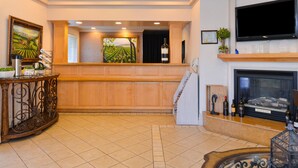 A lobby with a wooden reception desk, a fireplace, a television, and framed artwork.