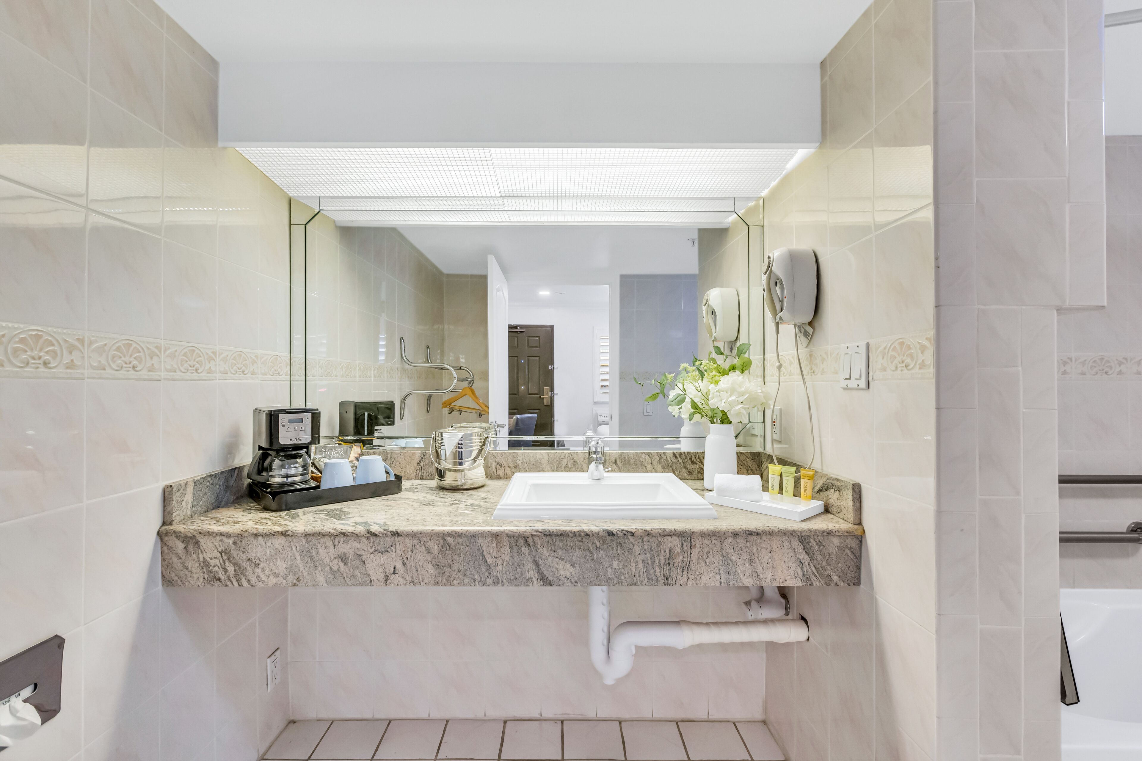 A modern bathroom with a marble countertop, a sink, a coffee machine, and a mirror.