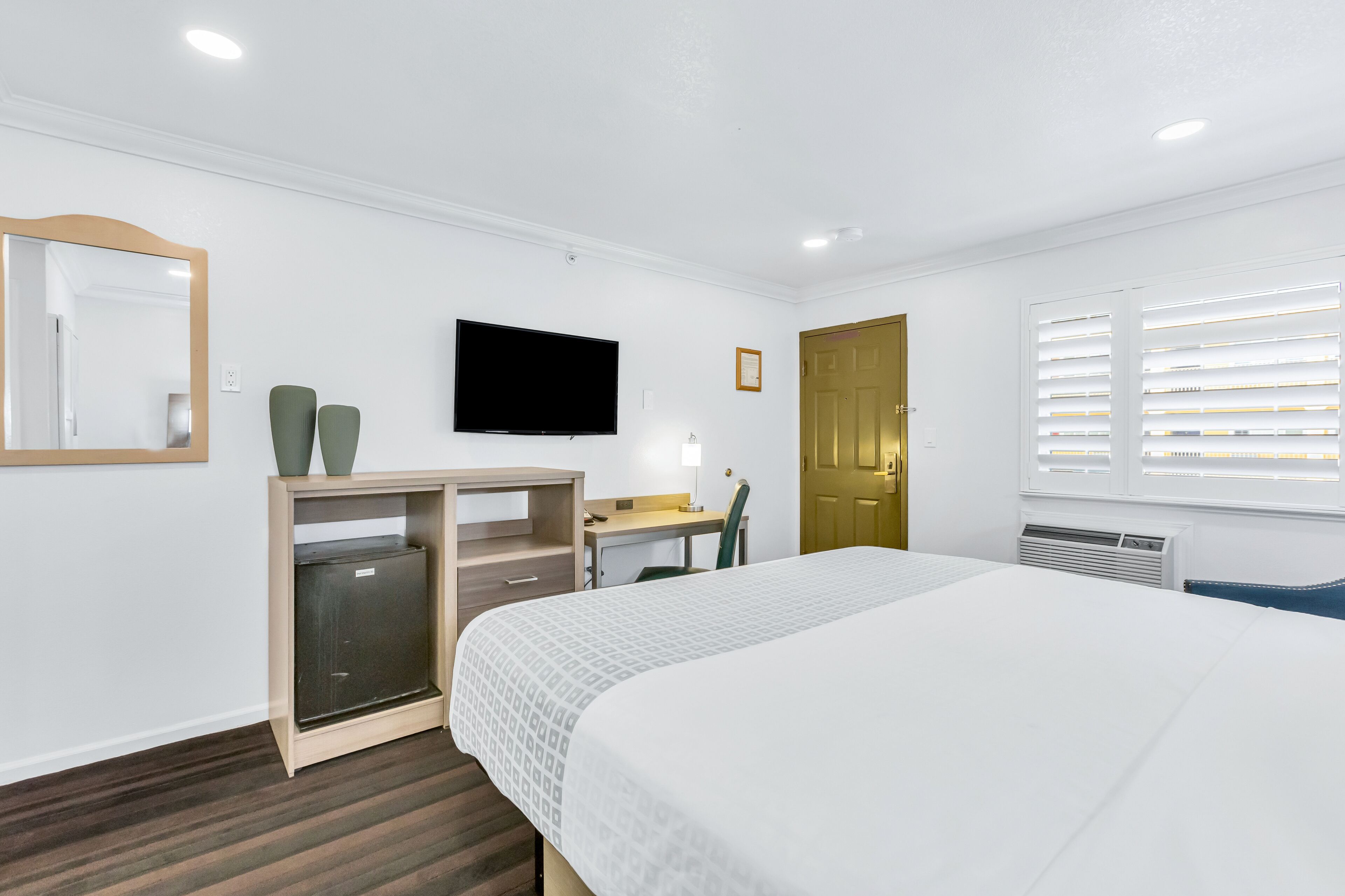 A hotel room with a bed, a desk with a chair, a television, a wardrobe, and a door.