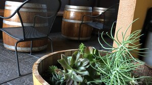 A rustic outdoor seating area with wooden barrels and metal chairs, a planter with various succulents, and a textured wall with a light fixture.