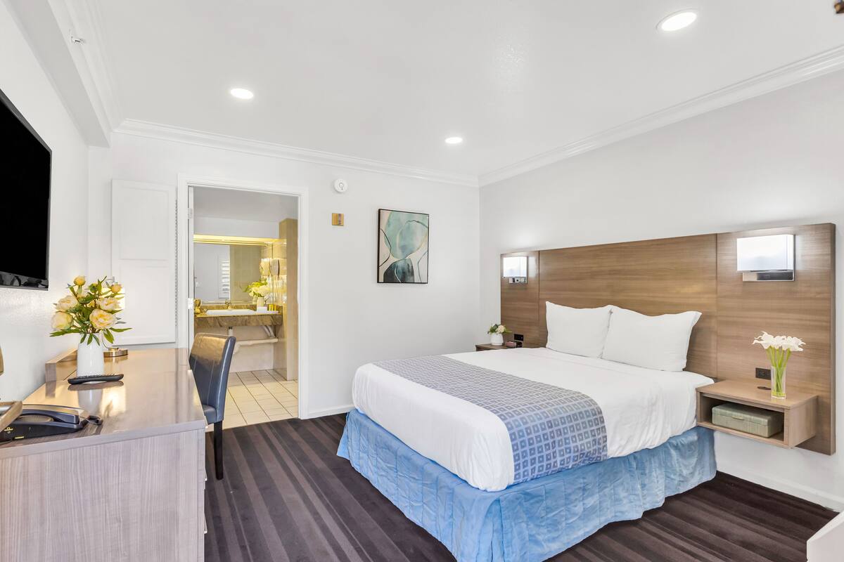A modern hotel room with a large bed, a desk with a telephone, and a mirror.