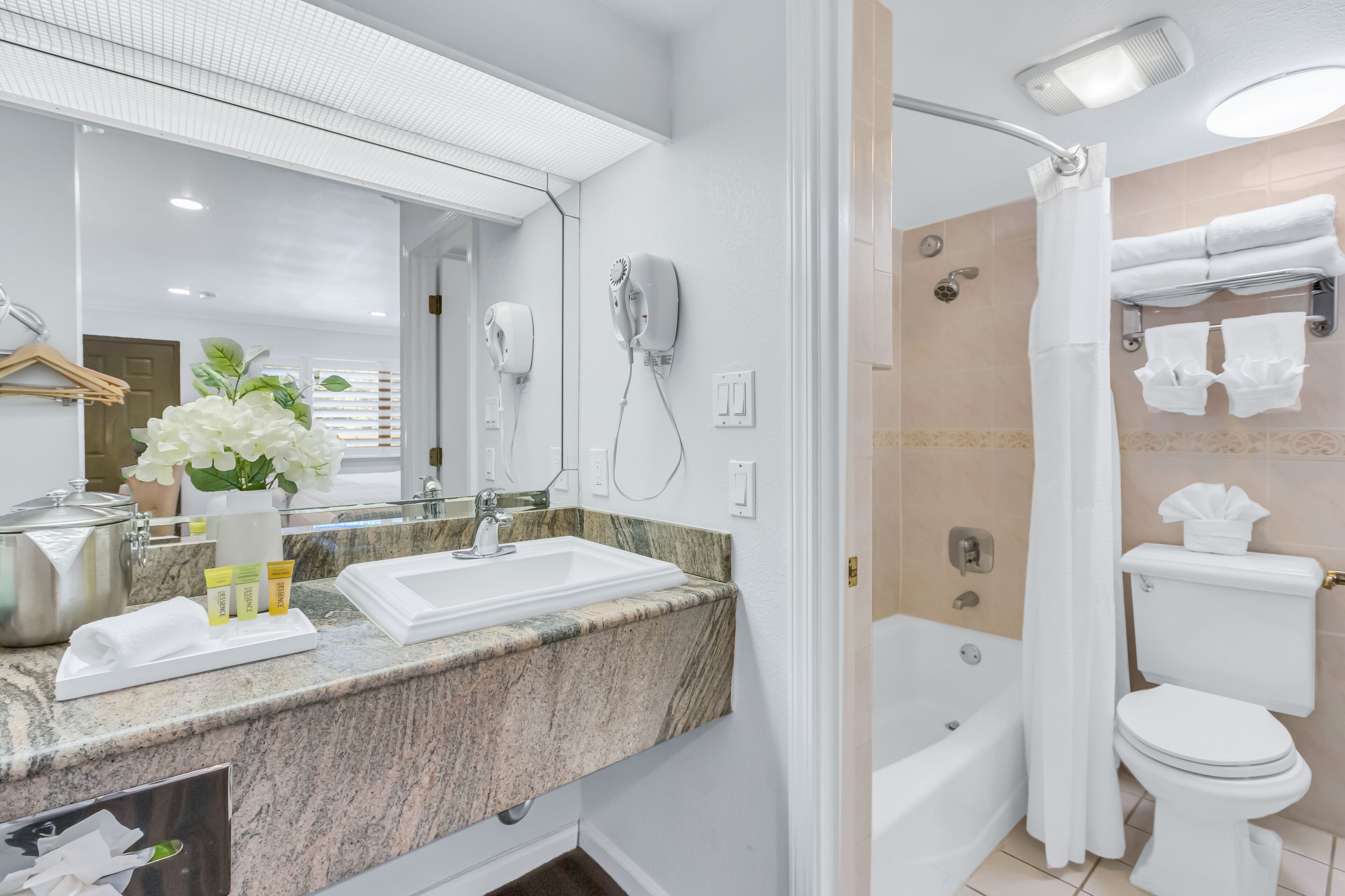 Un baño moderno con encimera de granito, un espejo grande, secador de pelo, ducha e inodoro.