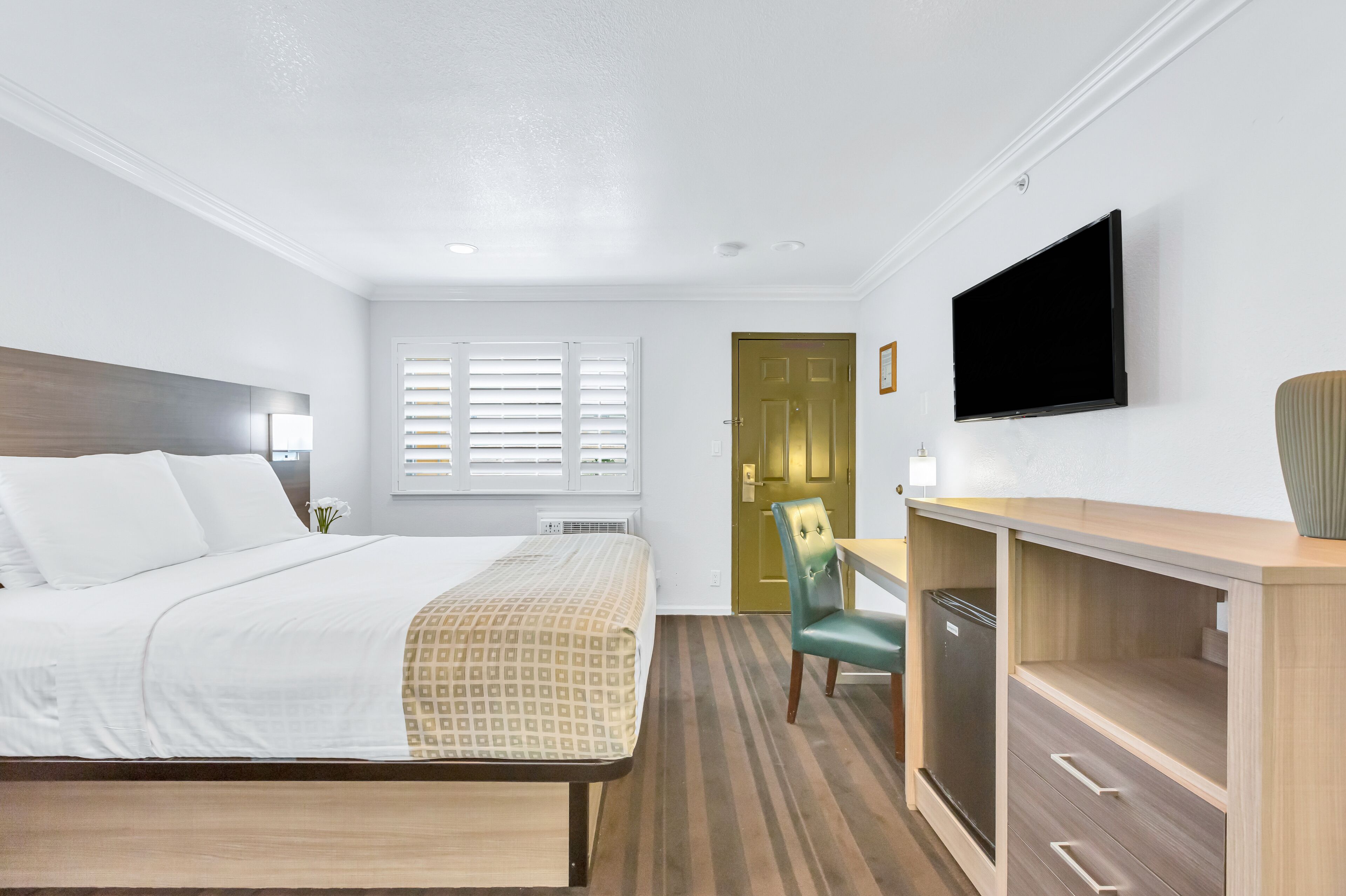 Una habitación de hotel con cama, escritorio, silla, televisor y puerta.