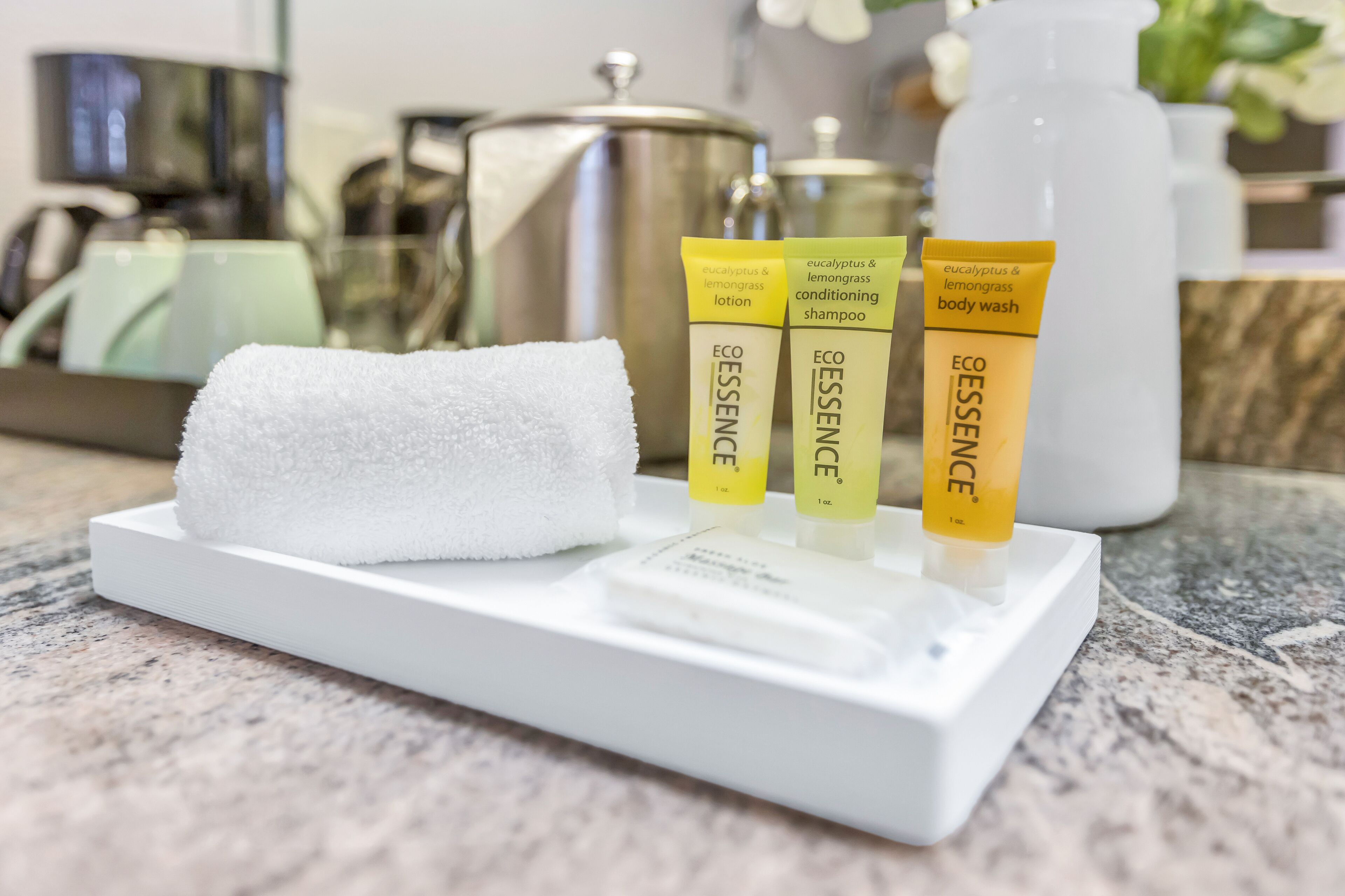 A white tray with three tubes of ESSENCE body wash and lotion, a white towel, and a white bottle on a marble countertop.
