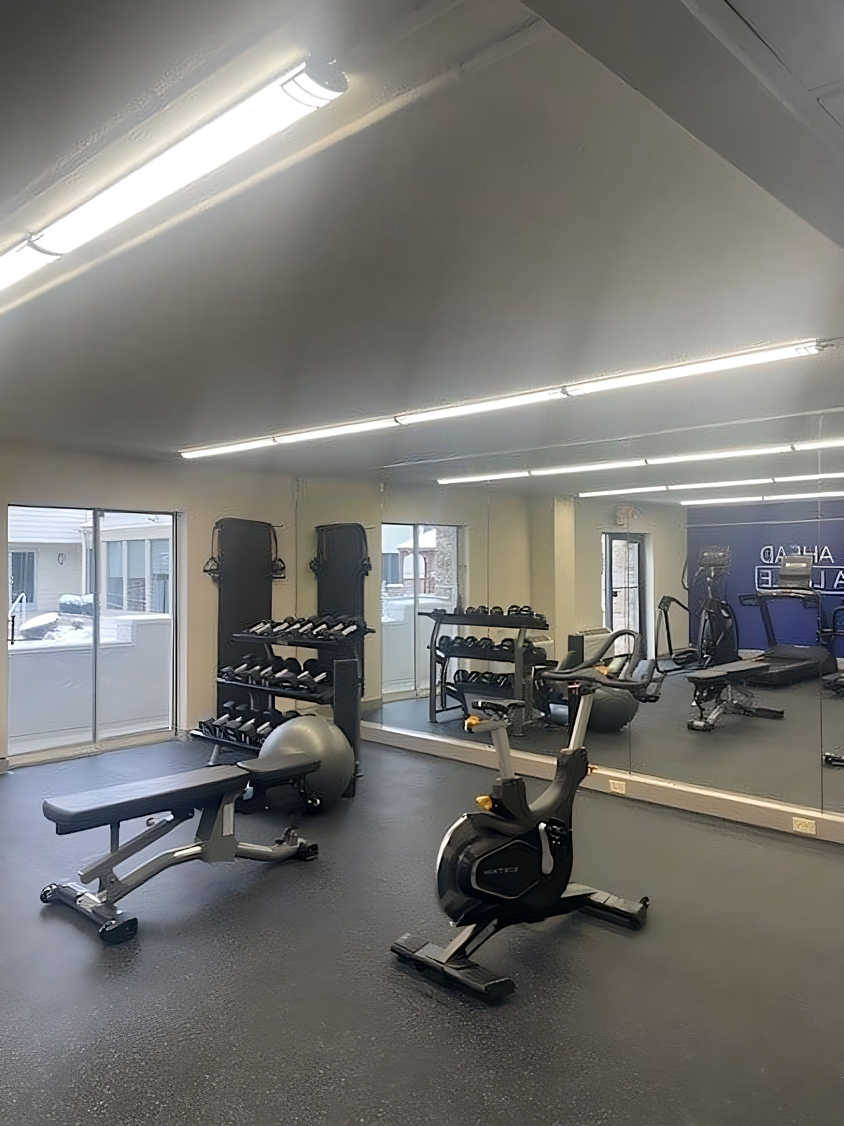 A gym with exercise equipment, a bench, and a mirrored wall.