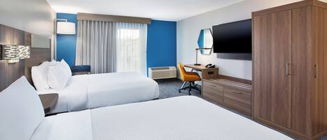 Quarto de hotel com duas camas, uma escrivaninha, uma cadeira, uma televisão e um guarda-roupa.
