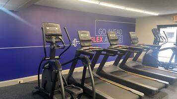 Une salle de sport équipée de tapis de course et d’appareils elliptiques, un mur violet orné de messages motivants et un luminaire au plafond.