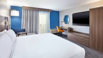 Una camera d'albergo con un letto grande, una scrivania con una sedia, una TV e una finestra con tende.