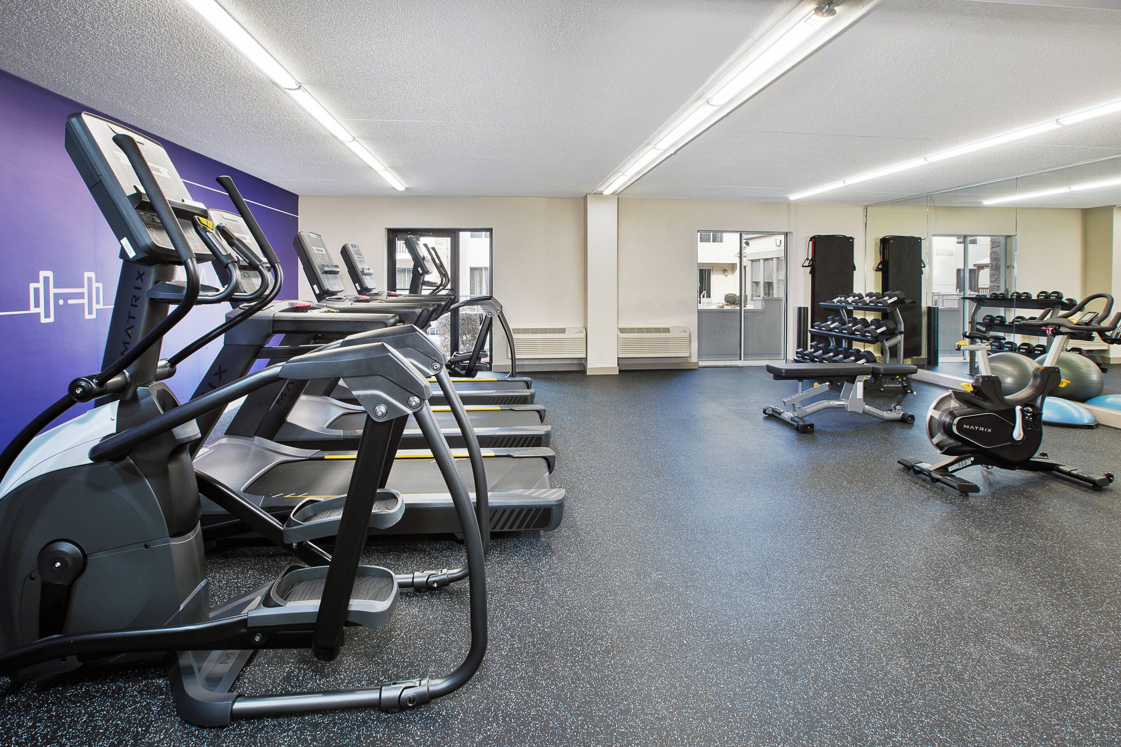 Un gimnasio con cintas de correr, bicicletas estáticas y pesas sueltas.