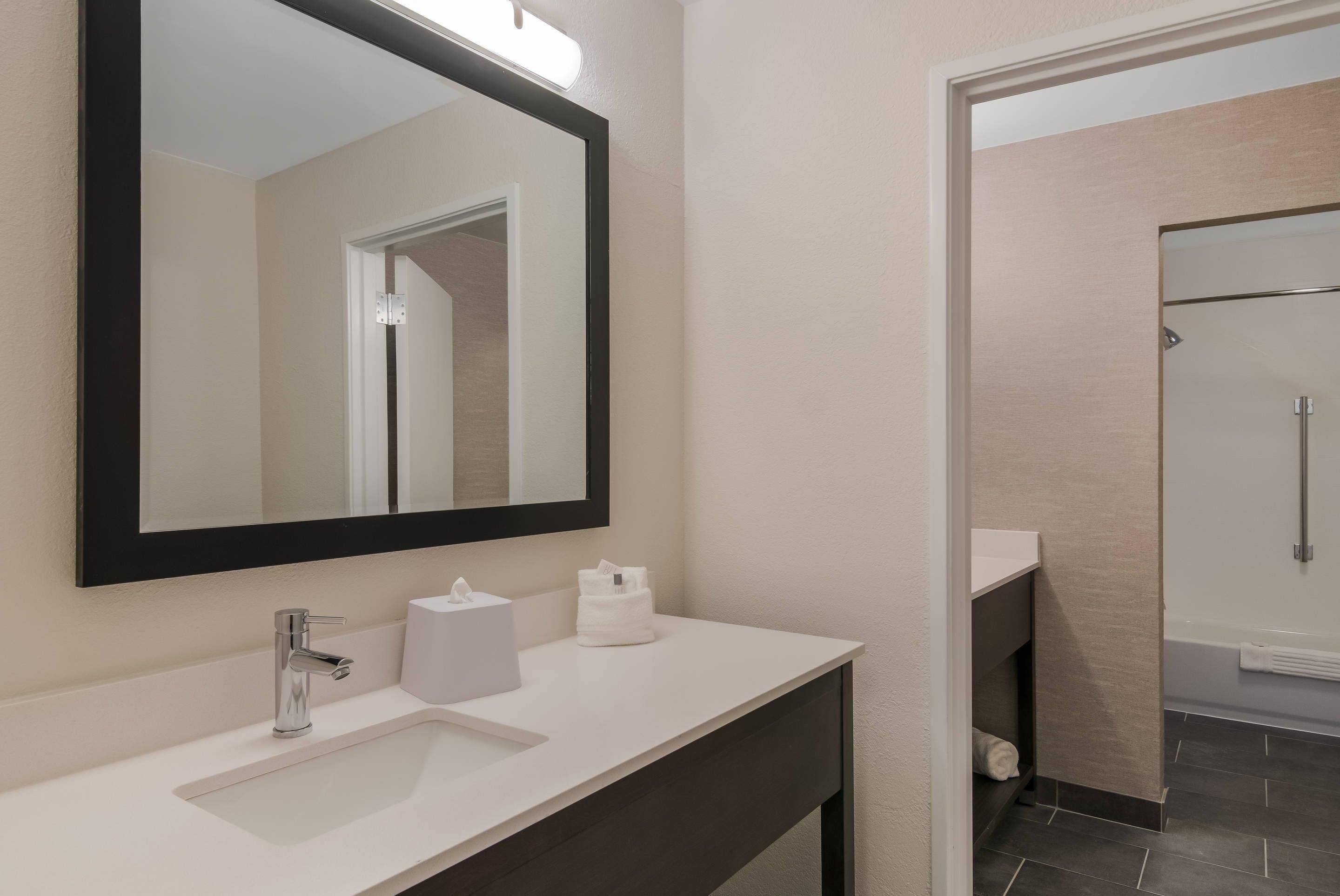 Un baño moderno con tocador blanco, un espejo grande y zona de ducha.