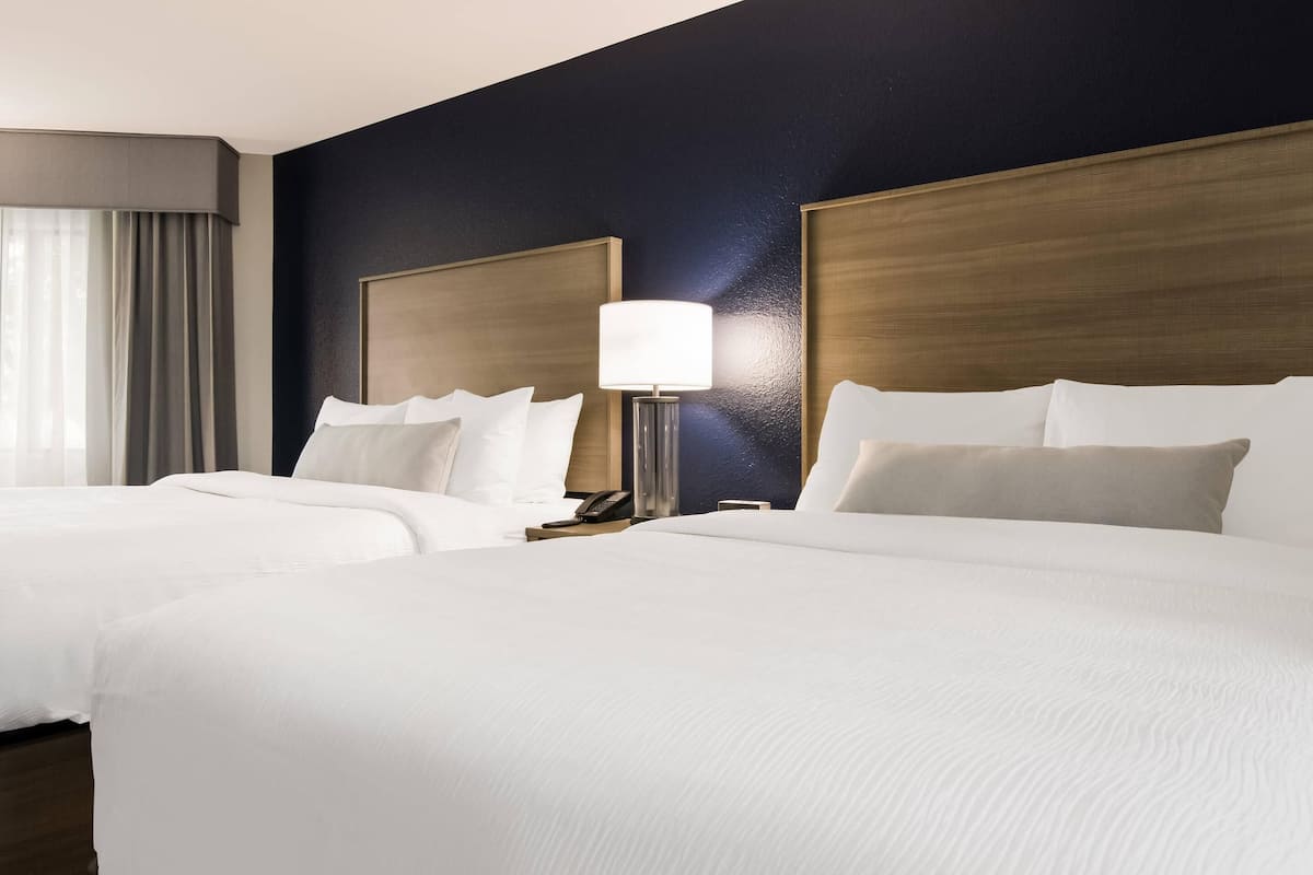 A hotel room with two beds, a nightstand, a lamp, and a telephone.