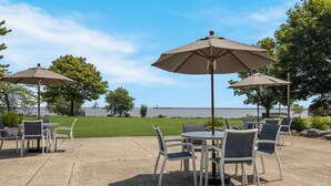 An outdoor patio with tables and chairs, large umbrellas, and a view of the water.
