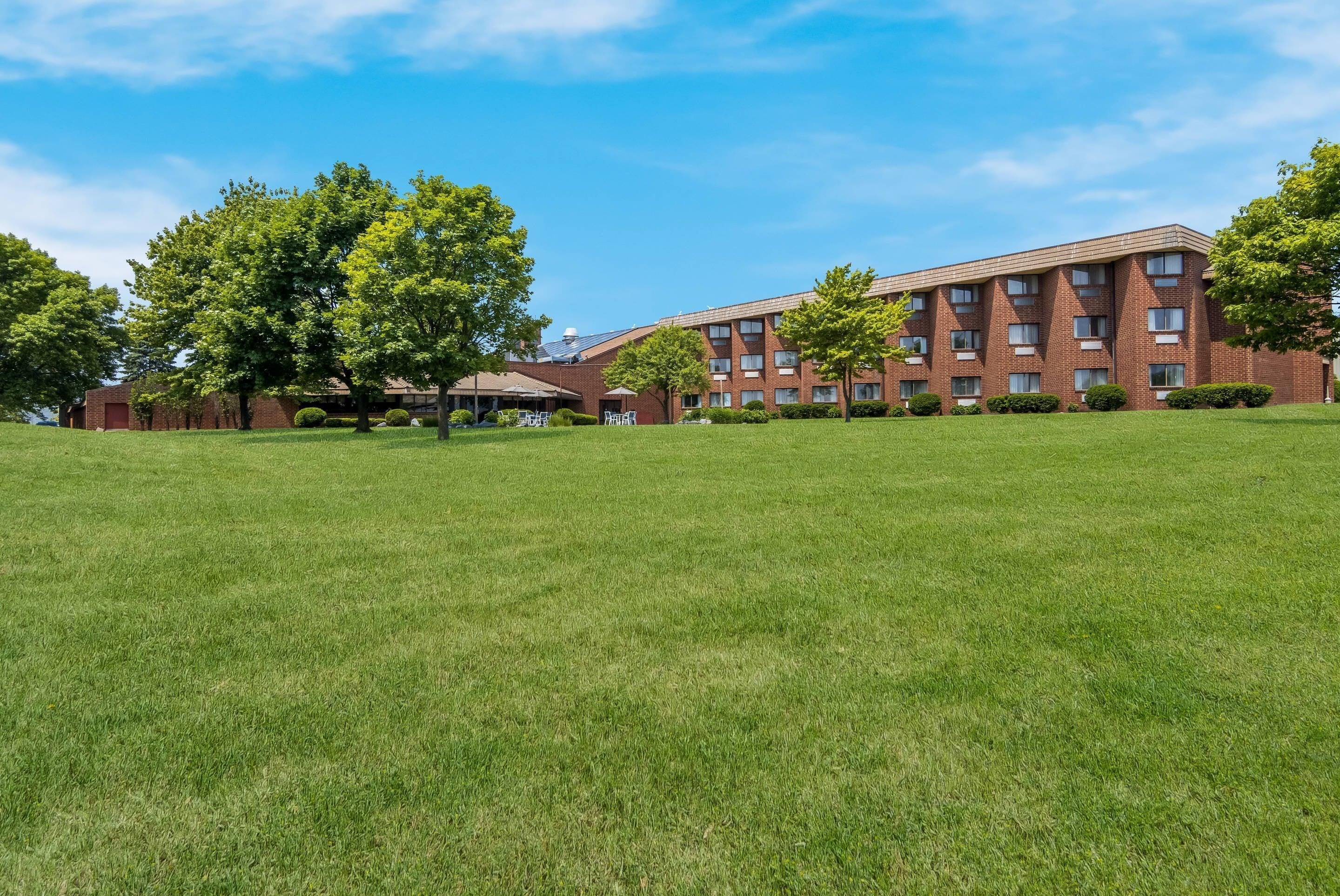 A multi-story brick building with a flat roof, surrounded by well-maintained grass lawns and trees.