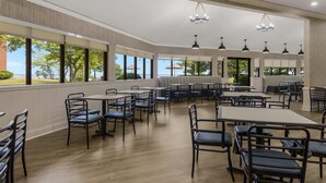 A spacious indoor dining area with multiple tables and chairs, large windows offering views of the outdoors, and pendant lighting fixtures.