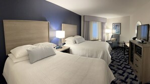 A hotel room with two beds, a desk, a TV, and a dresser.