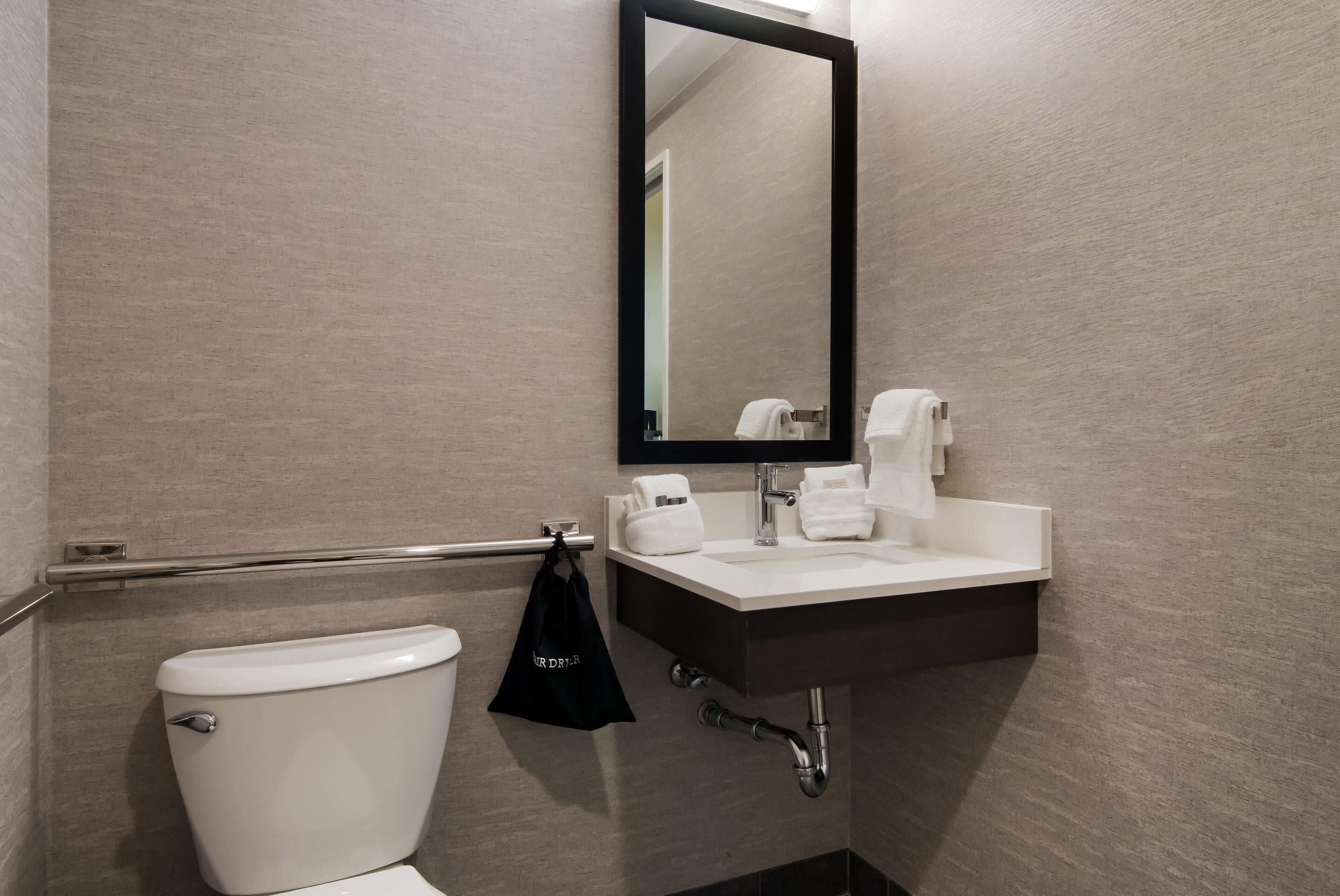 Une salle de bain avec des toilettes blanches, un miroir à cadre noir, un lavabo blanc et un porte-serviettes.