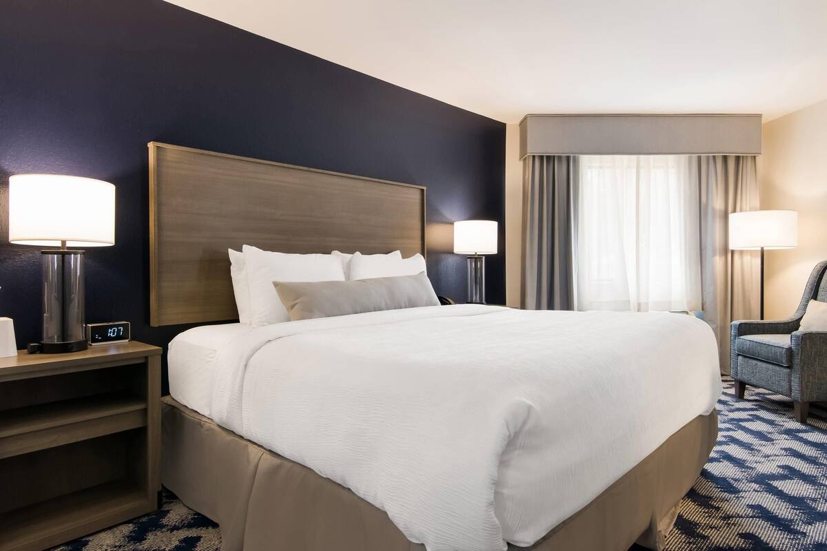 A hotel room with a large bed, two bedside tables with lamps, a chair, and a window with curtains.