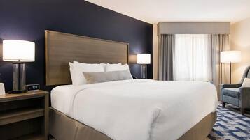 A hotel room with a large bed, two bedside tables with lamps, a chair, and a window with curtains.
