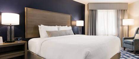 Una camera d'albergo con un letto grande, due comodini con lampade, una sedia e una finestra con tende.