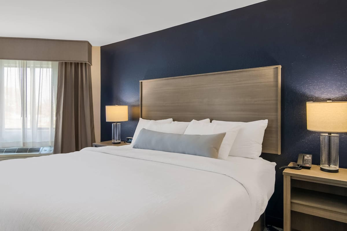 A hotel room with a large bed, two bedside lamps, a nightstand with a phone, and a window with curtains.