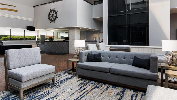 A modern lobby with a grey sofa, armchairs, and a large ship's wheel on the wall.
