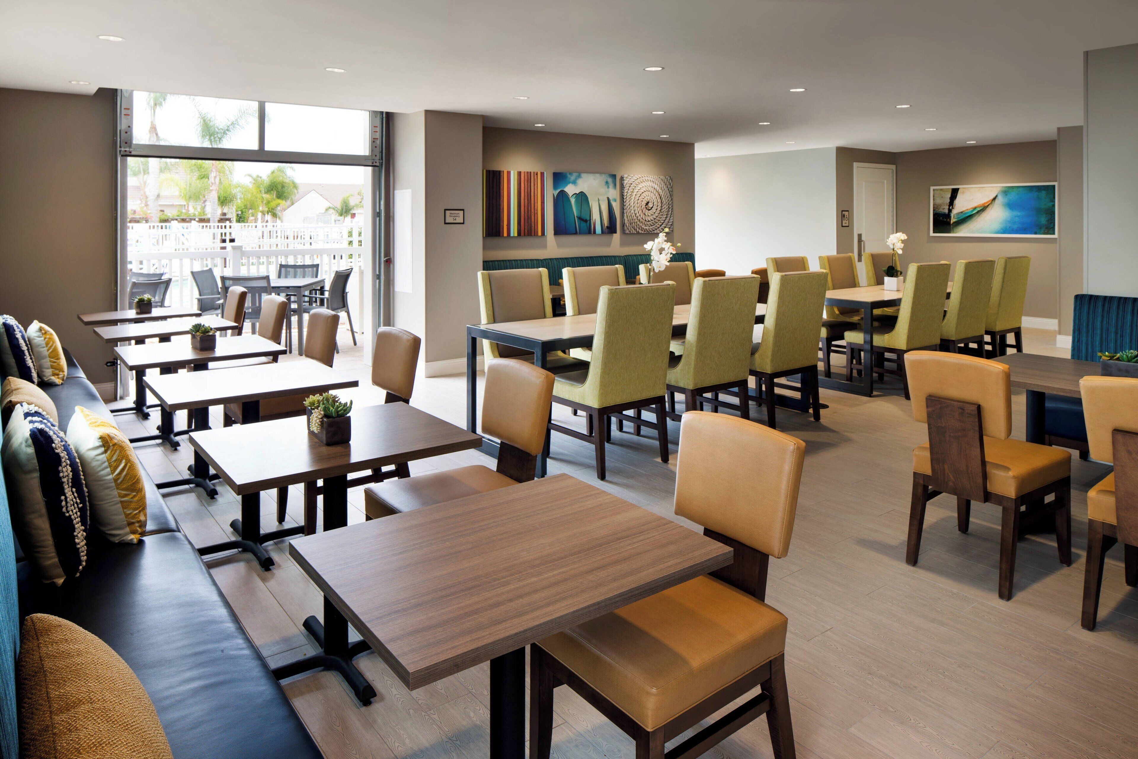 A modern dining area with multiple tables and chairs, a seating area with a sofa, and artwork on the walls.