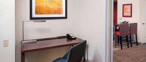 A hotel room with a desk, chair, and a framed abstract painting on the wall.