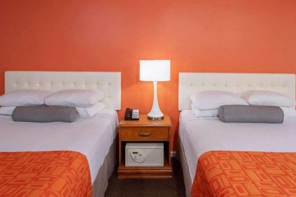 A hotel room with two beds, a nightstand with a lamp, a phone, and a safe.
