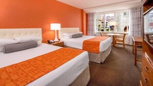 Habitación de hotel con dos camas, un escritorio y vistas a edificios a través de la ventana.