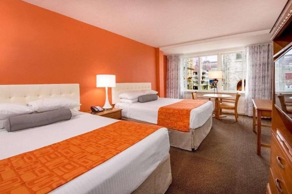 A hotel room with two beds, a desk, and a view of buildings through the window.