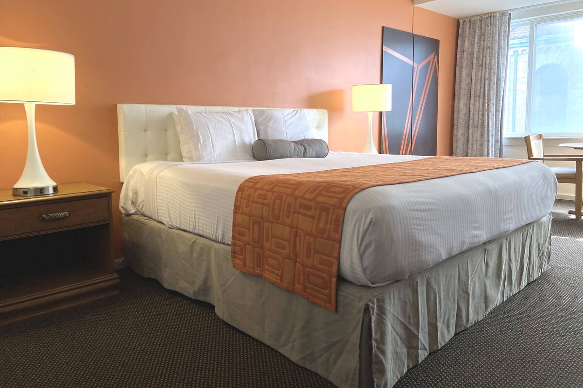 A hotel room with a large bed, two bedside tables, a desk, and a window with curtains.