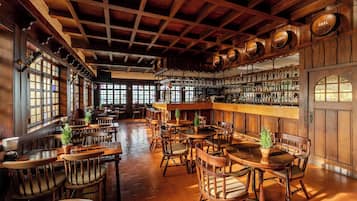 Una zona de bar con mobiliario de madera, barra y estanterías llenas de botellas.