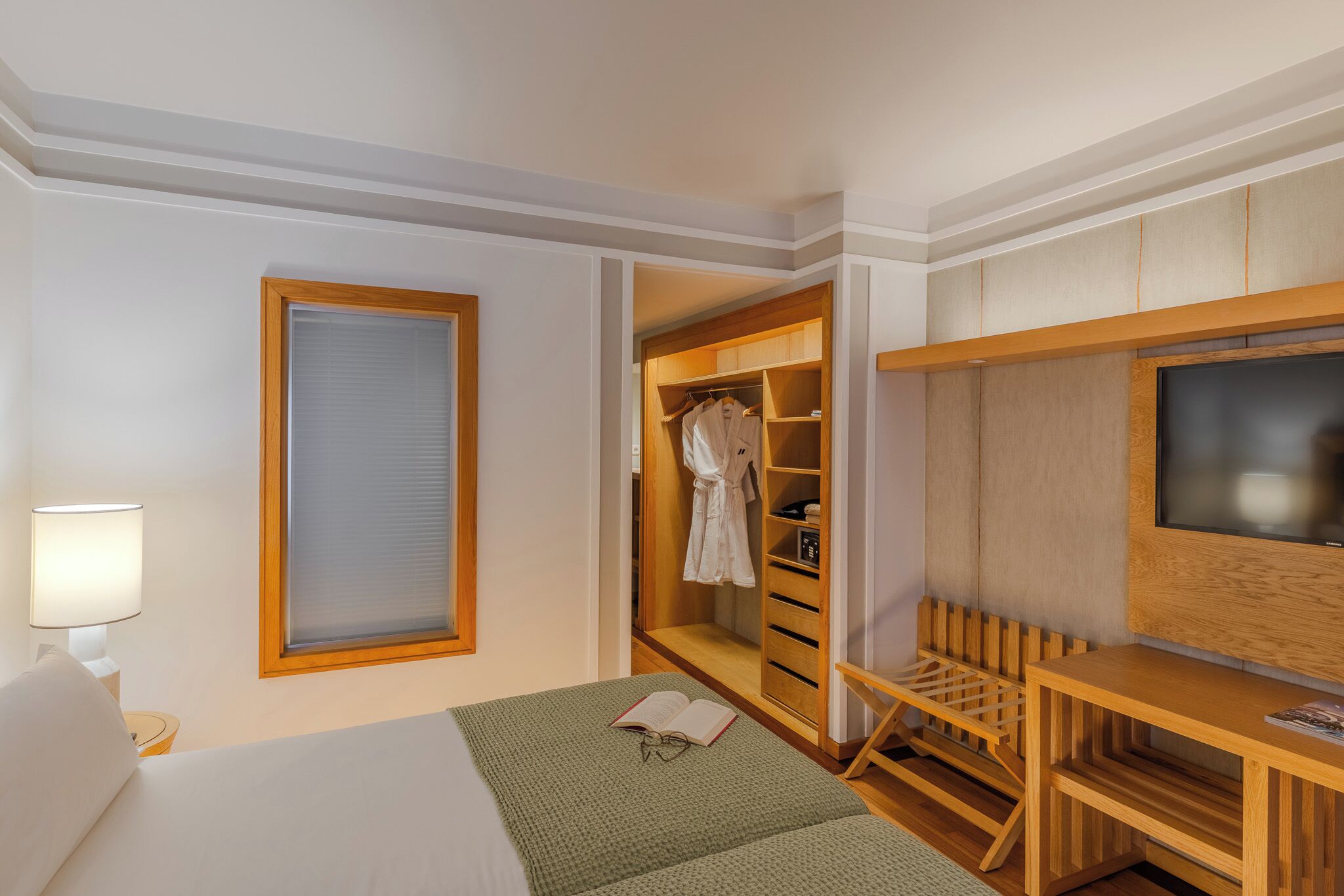 A hotel room with a bed, a TV, a wooden wardrobe, and a desk.