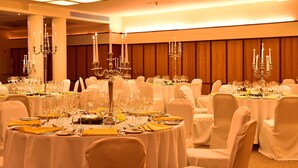 Une salle de banquet avec des tables rondes dressées pour un événement formel, agrémentée de chandeliers et de nappes blanches.