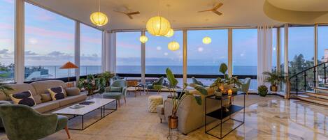 Un vaste espace de vie avec une grande fenêtre donnant sur la mer, un canapé, des fauteuils, une table basse et des plantes en pot.